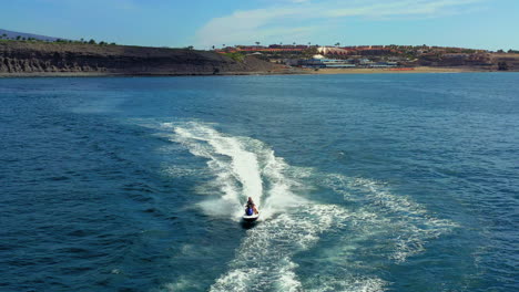 incredible aerial view, aerial bird's eye view of jet ski cruising in high speed in turquoise clear water sea beneath camera.