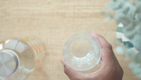 hand holding a glass of water, still life with a water bottle and eucalyptus plant.