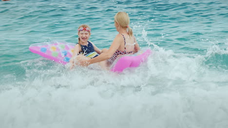 Enormes-Olas-Del-Mar-Juegan-Con-Un-Colchón-Inflable,-Una-Mujer-Con-Un-Niño-Pequeño-Ríe-Diviértete