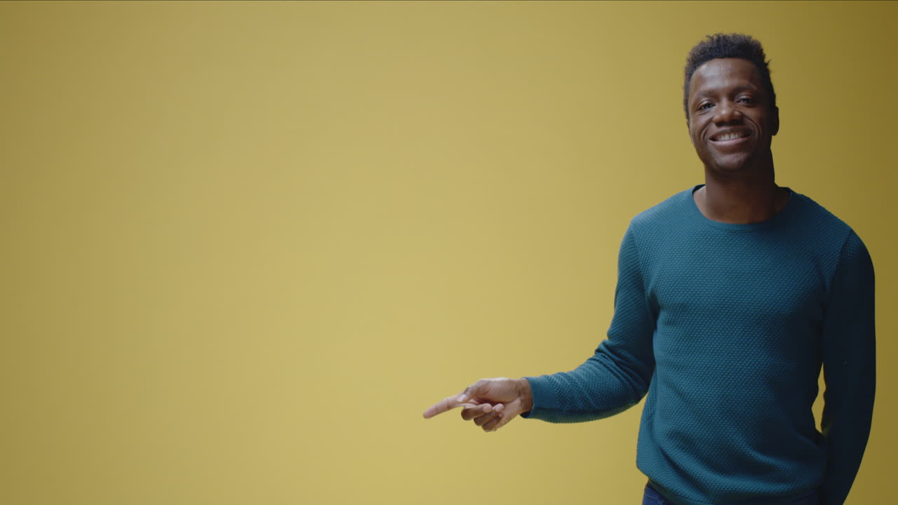 A smiling man points to the left on a yellow background