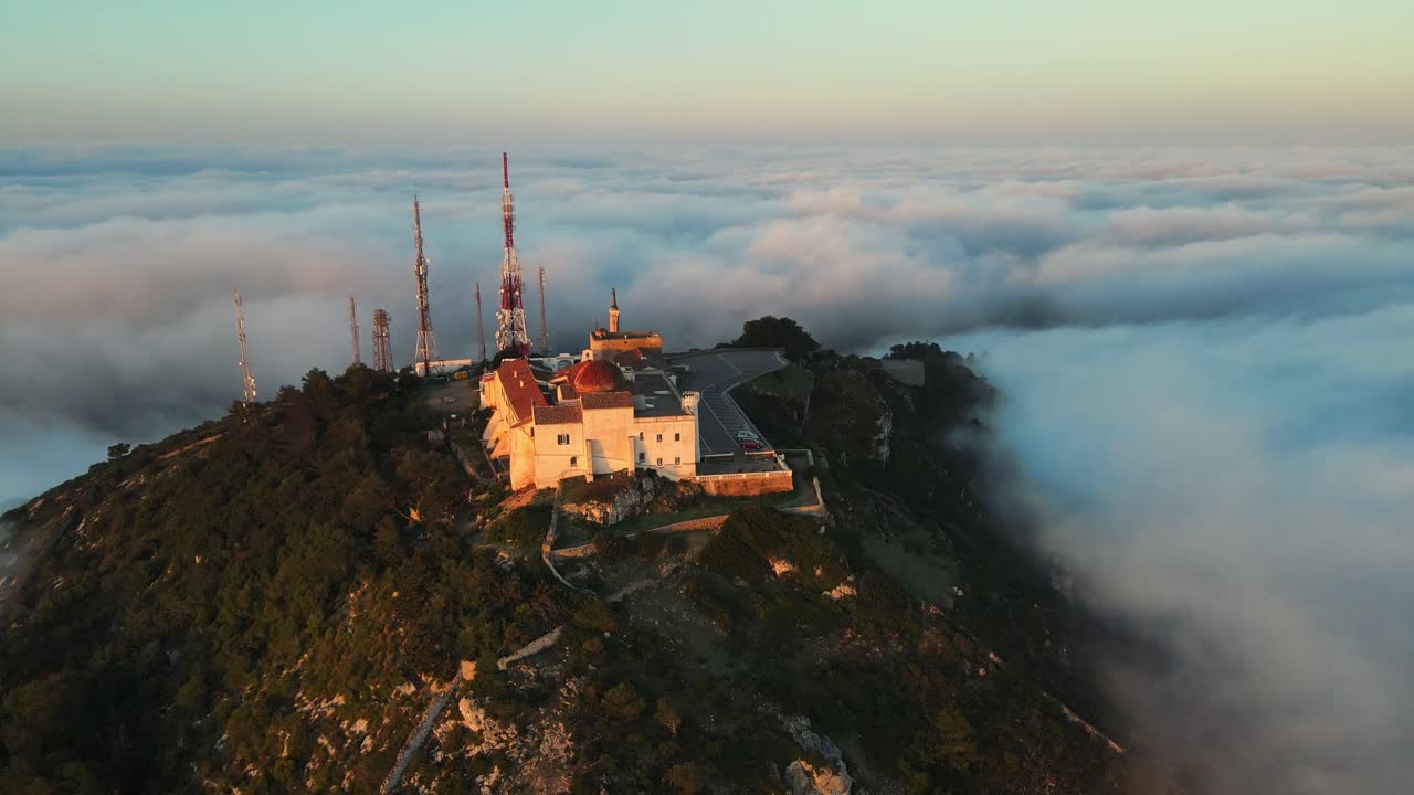 vuelo cinematográfico de drones que revela una montaña en la cima de una colina rodeada de niebla al amanecer