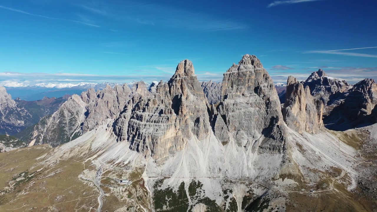 Spektakulær nærbillede droneoptagelse over de italienske Dolomitter. Viser tårnhøje, barske grå kalkstensbjergtinder og takkede klippeformationer, der står majestætisk under en klar blå himmel.
