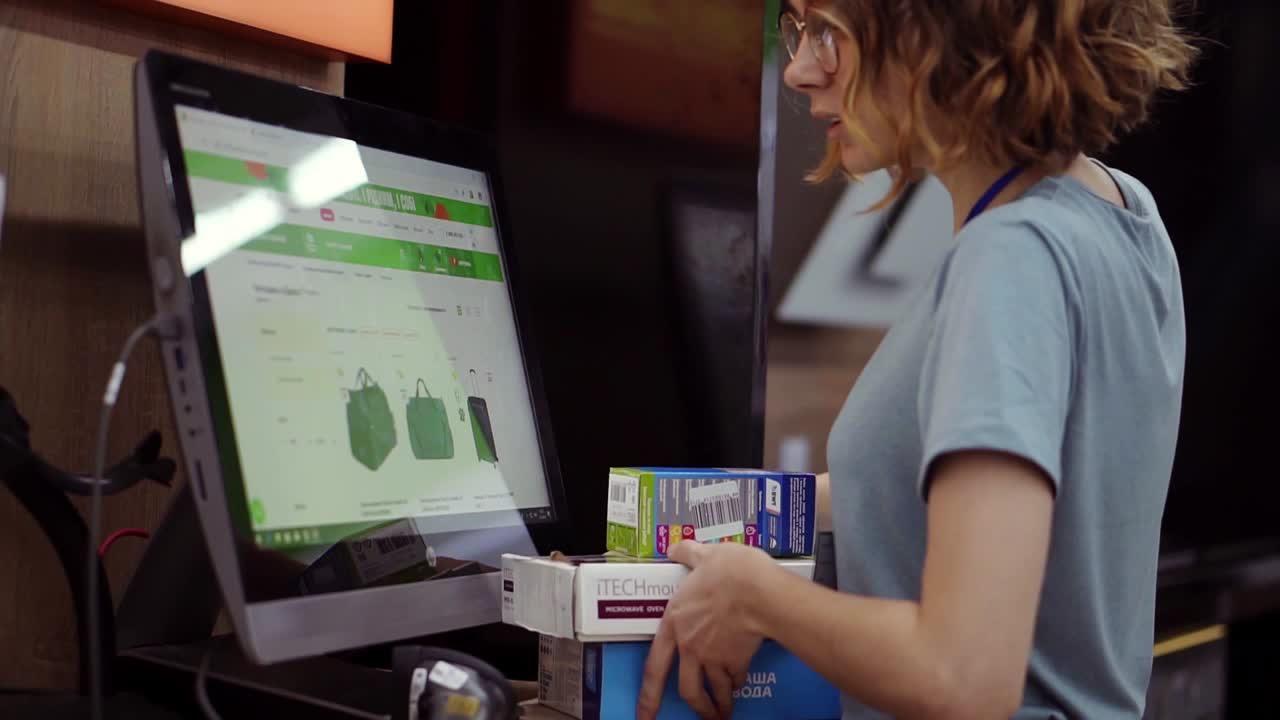 mujer delgada de cabello rizado vendedora-consultora en el departamento doméstico lleva y escanea por código de barras artículos de papelería en las cajas