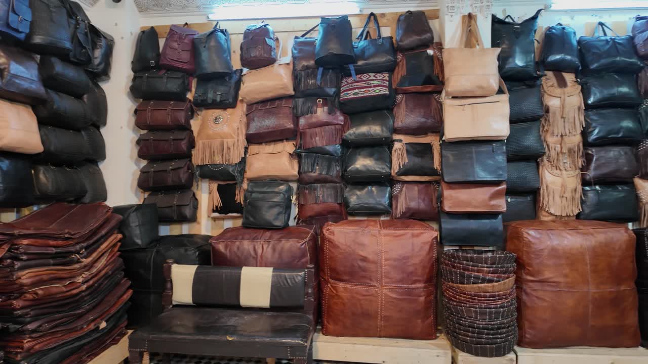Various leather bags and poufs displayed on shelves and stacked in a shop in Fes Medina Chouara Tannery, Morocco