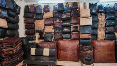various leather bags and poufs displayed on shelves and stacked in a shop in fes medina chouara tannery, morocco