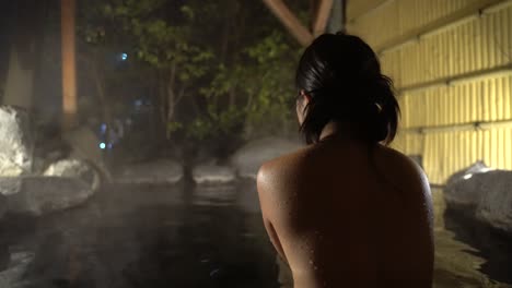 side-lit back view of naked female in outdoor hot spring bath