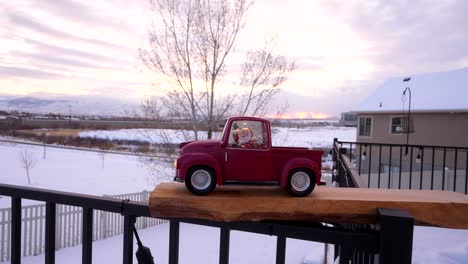 toy santa claus in a red christmas truck with a snow winter background at sunset - parallax motion