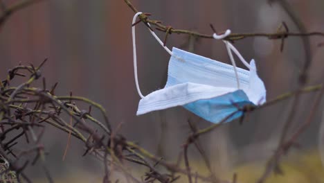 medizinische einweg-blauschutzmaske schwebt im wind auf stacheldraht, coronavirus-kovid-19-virusabfall