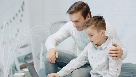 relaxed father and son sitting in front of laptop computer in luxury house