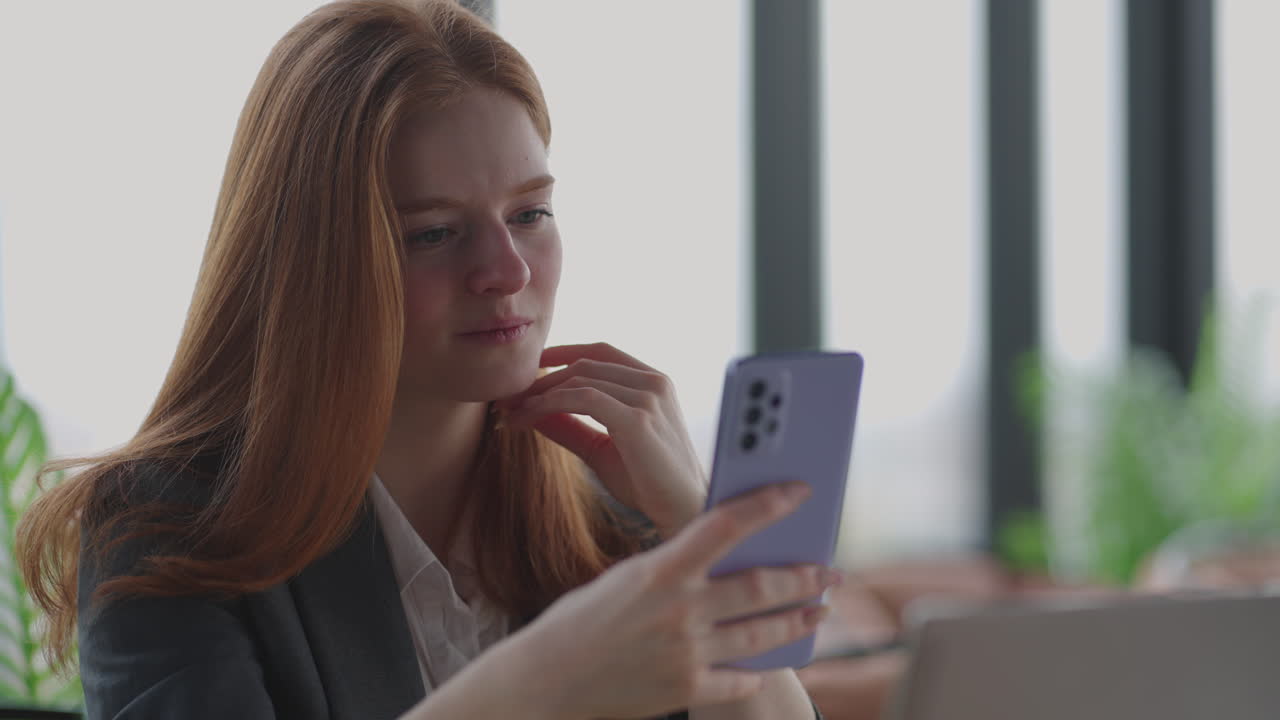 donna gioiosa sta lavorando in ufficio e visualizza i social media nel suo smartphone sorridendo quando legge notizie positive