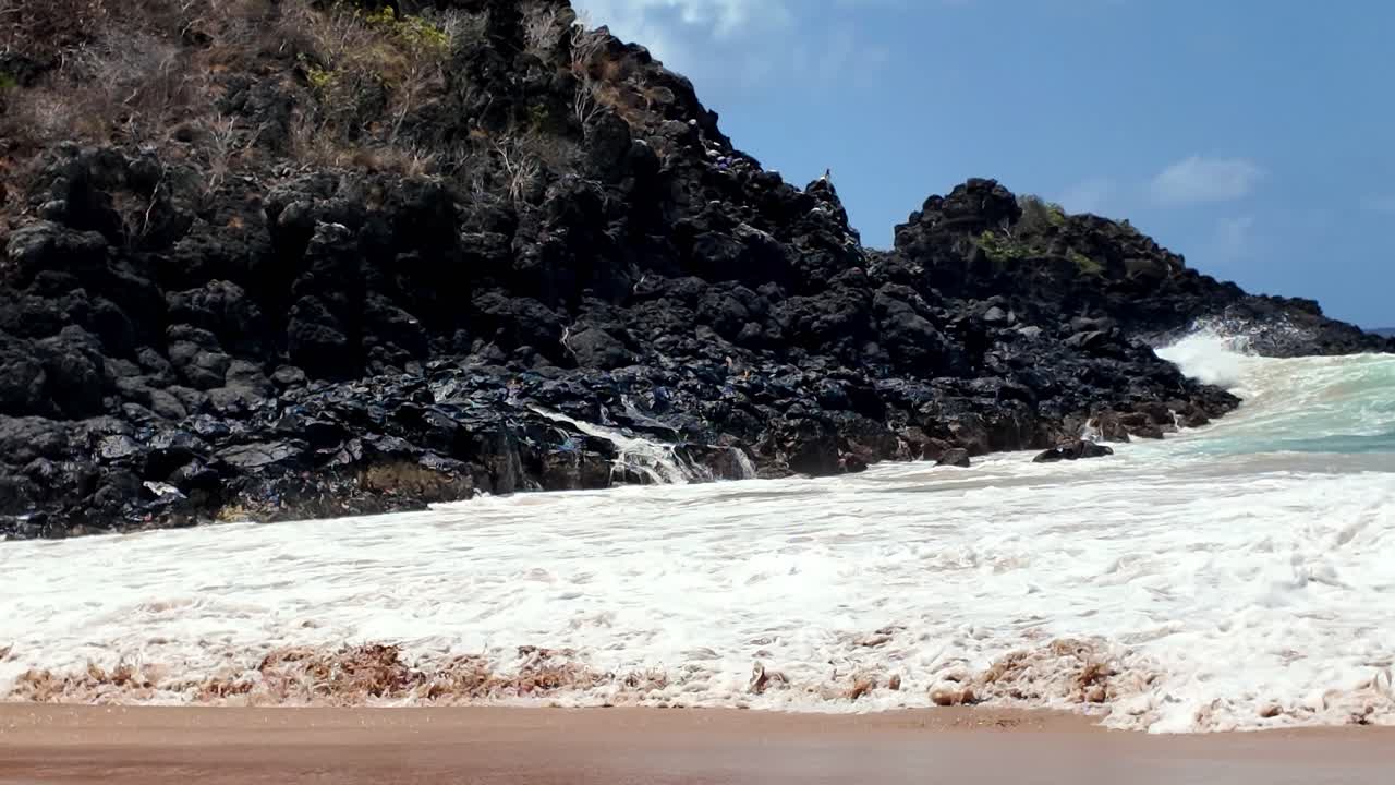 Powerful waves hit large dark volcanic rocks along Noronha’s dramatic coastline