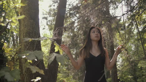 medium shot of beautiful asian woman in black exploring sunny forest, slowmo