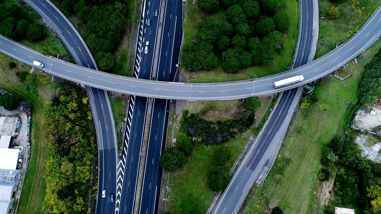 프랑스의 3개의 고속도로 교차로 위의 공중 전망: 도로 주변의 집과 잔디, 도로에서 운행되는 자동차와 트럭.