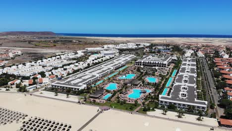 Aerial-View-Of-Bikini-Beach-Parasols-With-Resort-And-Swimming-Pools-In-Background