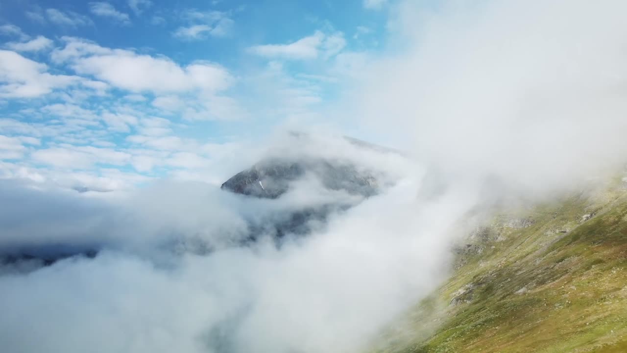 Aerial drone footage slowly flying forward in the middle and through white soft and fluffy clouds over Sweden green grassy and mossy rocky hillside landscape during a sunny day, mountain visible also.