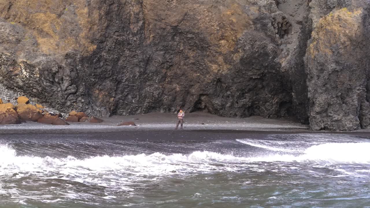 un hombre solitario en la playa de arena negra en islandia mira hacia el horizonte