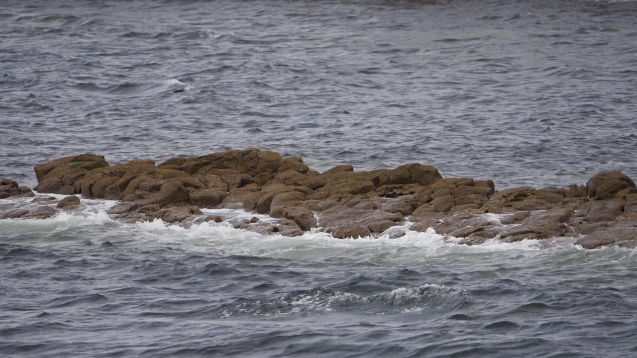 Onde oceaniche al rallentatore si infrangono sulle aspre rocce costiere lungo la costa occidentale della Scozia, creando un paesaggio marino suggestivo con texture naturali, acqua increspata e un'atmosfera marittima malinconica.