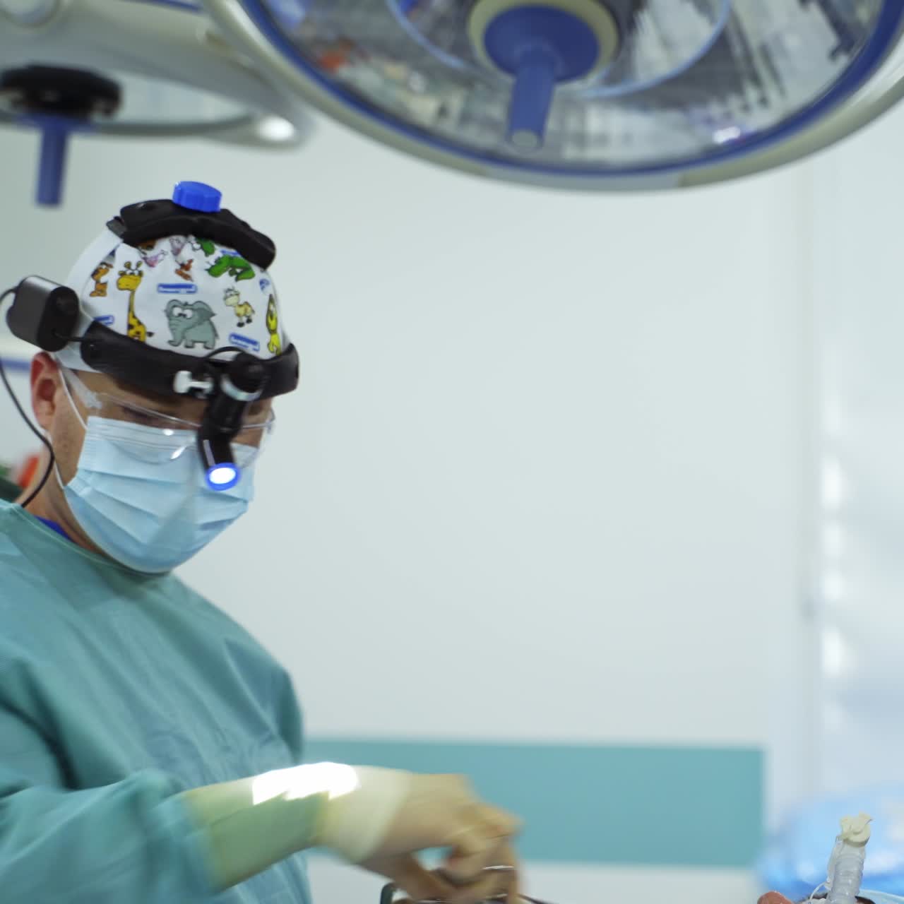 Surgeon in mask and device glasses holding forceps with sponge. The doctor applies antiseptic on the patient's face for sterility at operation
