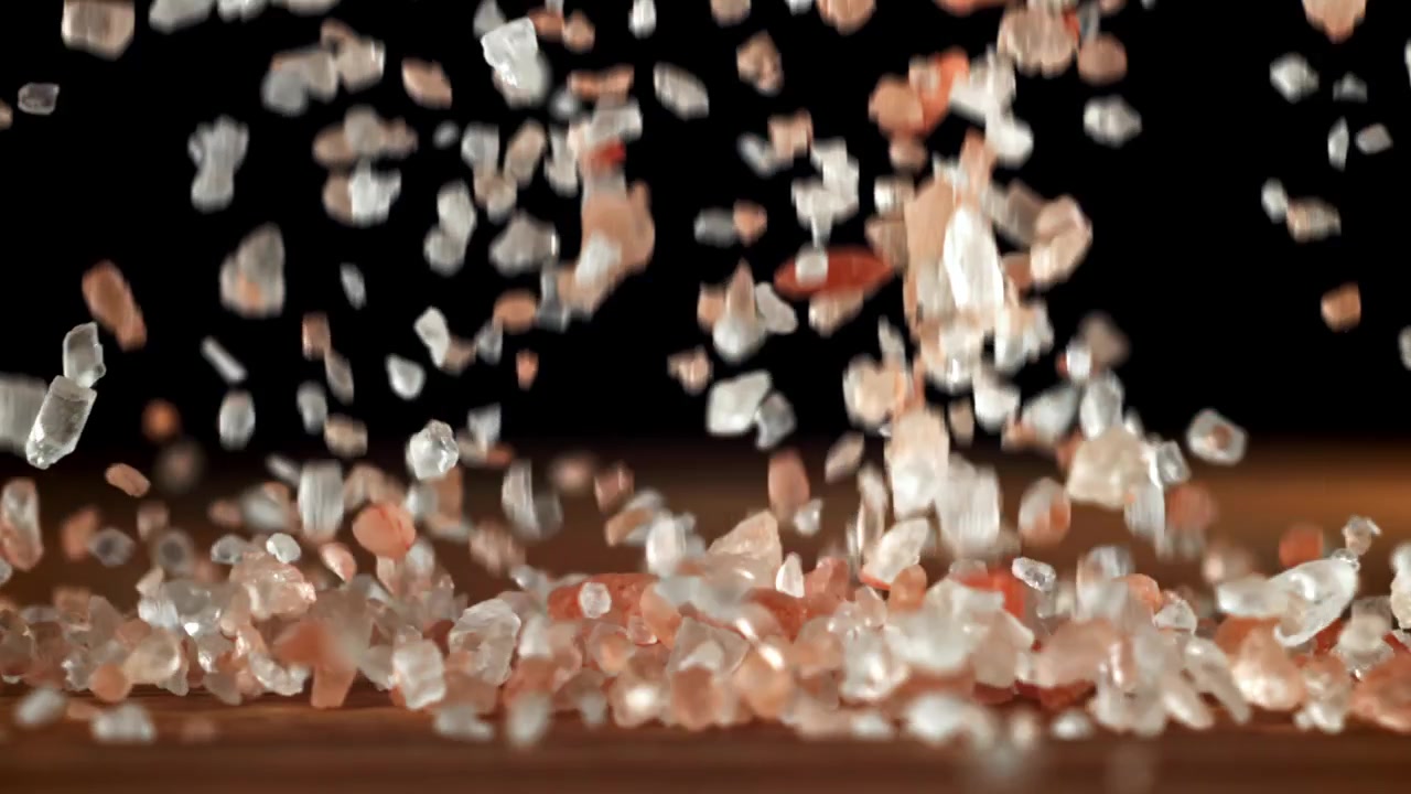 Sale rosa e bianco dell'Himalaya che cade su una superficie di legno al rallentatore