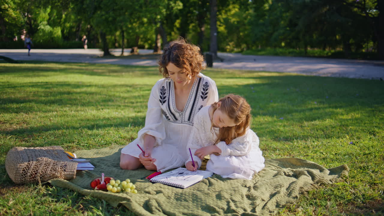 Woman girl talking picnic sitting sunny green lawn. Mother daughter drawing
