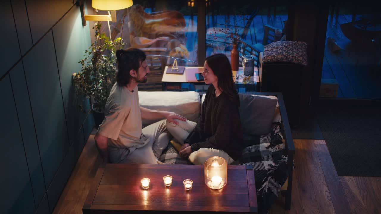 романтический вечер: парень и девушка сидят на диване в комнате, освещенной свечами. парень делает девушке предложение, она соглашается, и они обнимаются