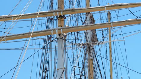 tall ship rigging gently swaying, backlit against a clear blue sky, showing three masts and crow's nest