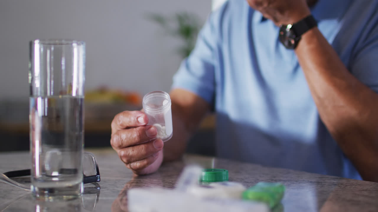 un hombre de dos razas con un vaso de agua tomando pastillas.