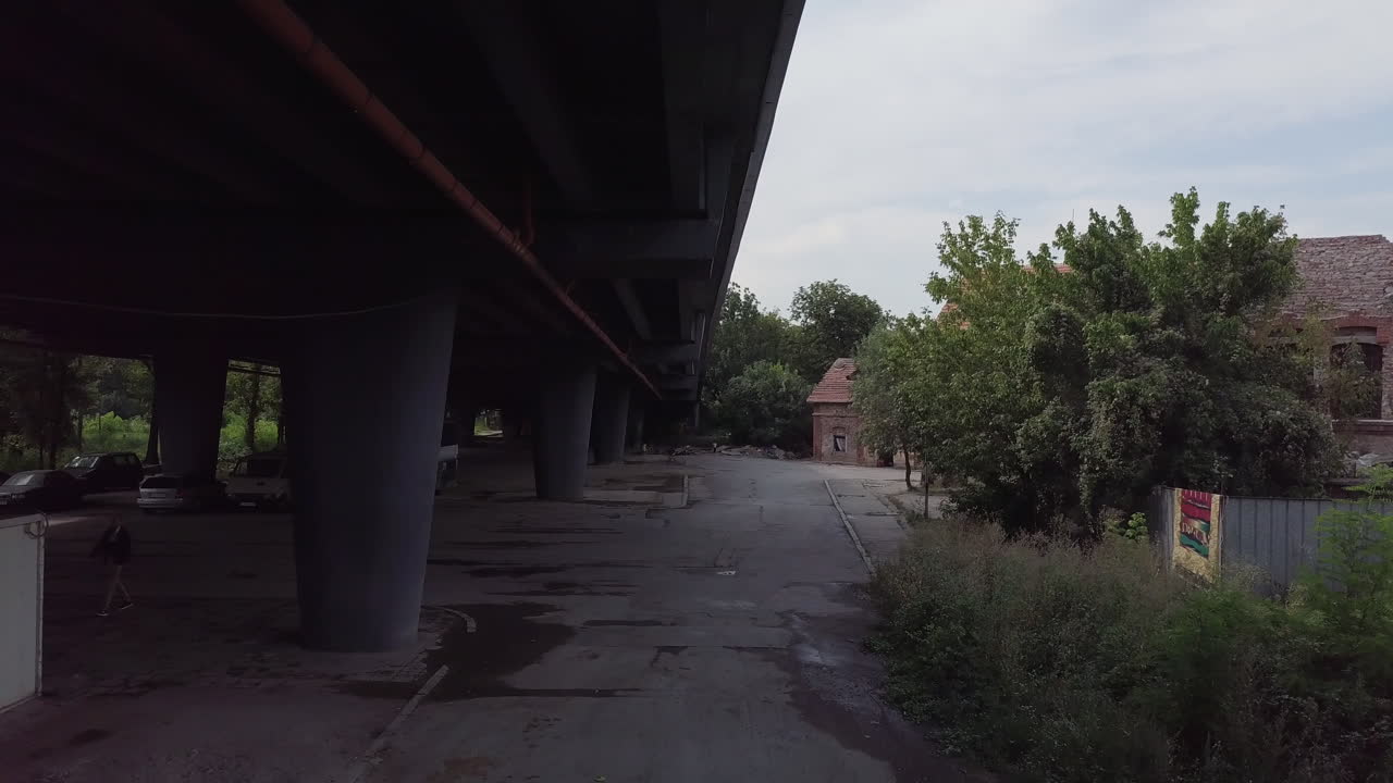 Drone flying under bridge near half destroyed house