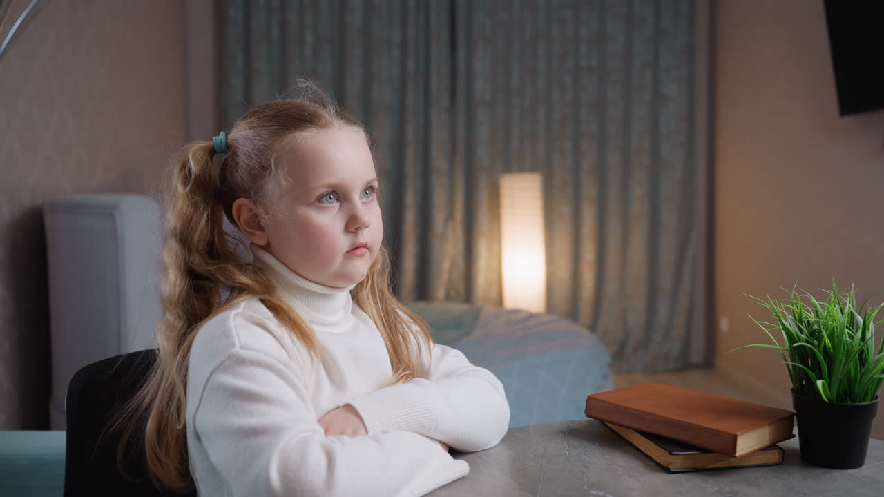 Bambina seduta a un tavolo in un interno accogliente, che tiene in mano un quaderno con la mano della madre visibile; la bambina è concentrata sull'apprendimento e sulla creatività, atmosfera familiare calorosa, luce soffusa di una lampada, pianta, supporto genitoriale