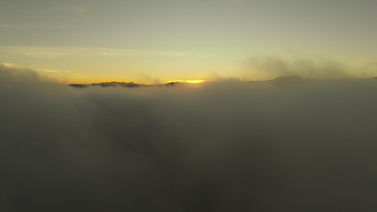 Drone captures golden sunrise as light emerges above horizon over a vast sea of clouds