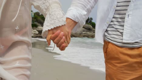 sección media de una pareja caminando de la mano en la playa 4k