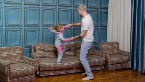 Happy-funny-family-father-and-child-kid-daughter-dancing,-jumping-on-sofa,-listening-music-at-home