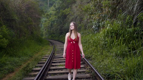 young girl in red dress walking along the railway tracks