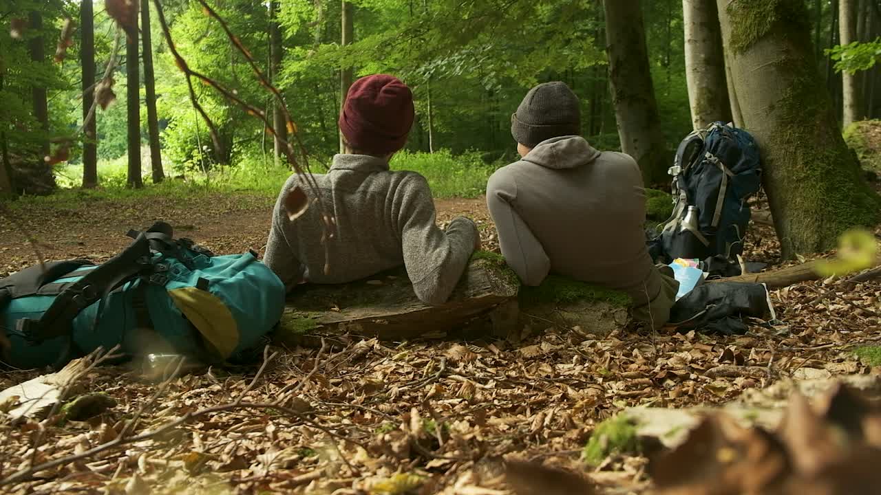 This footage beautifully captures the quiet companionship of a shared adventure. Two backpackers rest side-by-side, immersed in the serenity of the forest