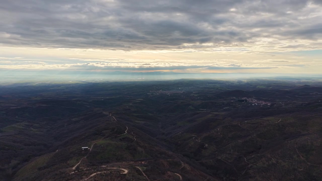 Imagens de drone sobre Kastaneri, Kilkis, Grécia, capturando amplas vistas panorâmicas de uma vila de montanha cercada por florestas com cores de outono e uma paisagem rural suave em tons de marrom-esverdeado