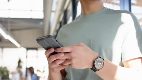 Holding smartphone, man in casual attire checking messages in modern interior, at office
