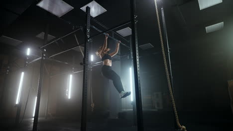 una mujer joven y deportiva está colgando de una barra transversal en el gimnasio y haciendo ejercicios de fuerza en el gimnasio