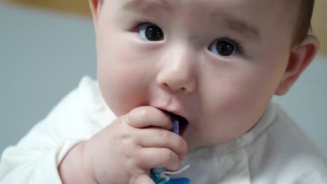 lindo bebé tratando de comer una pulsera colorida y sonriendo a la cámara, de cerca