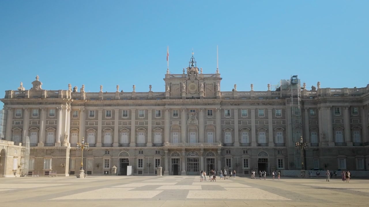 Un'ampia inquadratura del maestoso Palazzo Reale di Madrid in Spagna, con turisti che passeggiano nel cortile sotto un sole splendente. Perfetto per documentari di viaggio e contenuti sul turismo europeo.