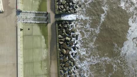 dolly drone shot up the coastline showing the boulder barriers cover by the waves