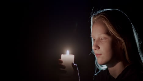 retrato de un niño mirando una vela ardiendo en la oscuridad. vista lateral