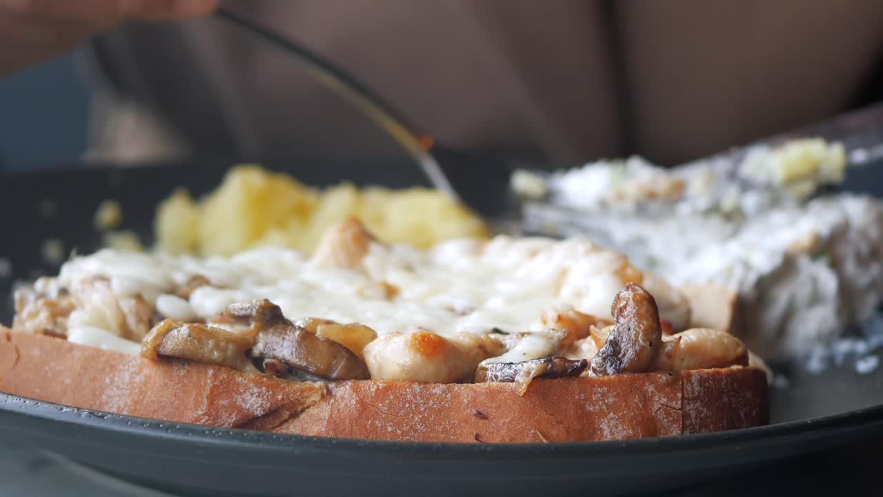 Primo piano di una persona che mangia un toast salato con funghi, pollo e formaggio fuso