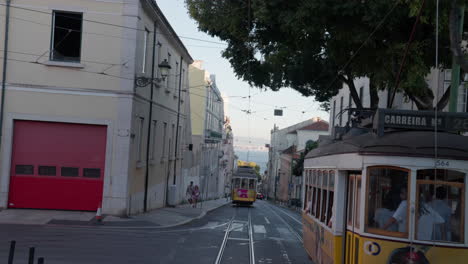 two yellow and white electric trolleys move along parallel tracks, carrying locals and tourists through the historic streets of lisbon, portugal, surrounded by narrow lanes and classic architecture.