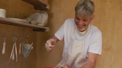 un uomo caucasico anziano sorridente che indossa un grembiule che fa ceramica sulla ruota del vasaio nel suo laboratorio