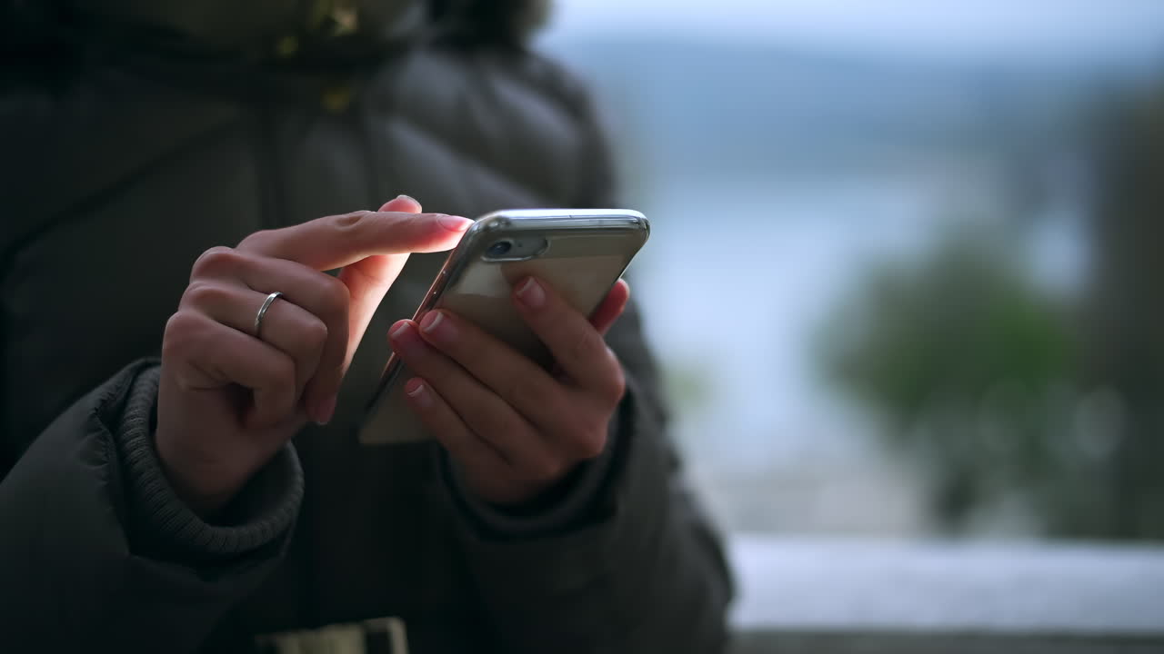Una persona interagisce con il proprio smartphone al crepuscolo. L'ambientazione offre una vista rilassante dell'acqua sullo sfondo, creando un'atmosfera di pace.