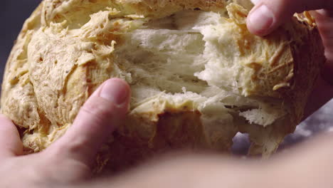 hands breaking apart fresh baked bread, close up