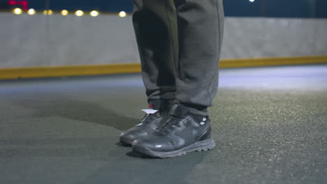 vista de la pierna de un hombre con zapatillas de deporte pateando una pelota de fútbol en un campo urbano iluminado bajo luces nocturnas, con la pelota estacionaria frente al poste de la portería