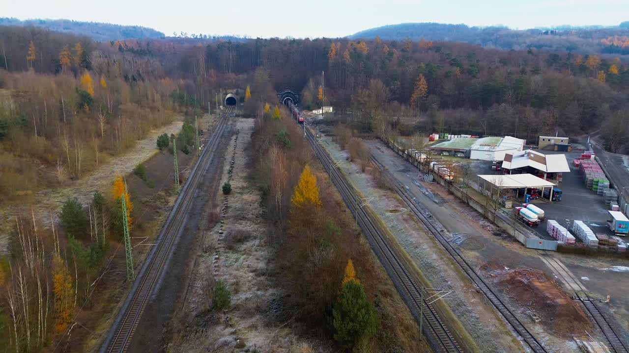 Red regional train approaching twin railway tunnels in frosty winter landscape captured from aerial perspective