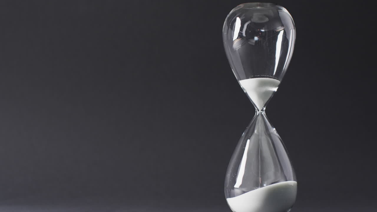 Video of hourglass with sand pouring, copy space on black background