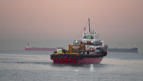 un remolcador sale al mar con portacontenedores en el fondo durante un colorido amanecer